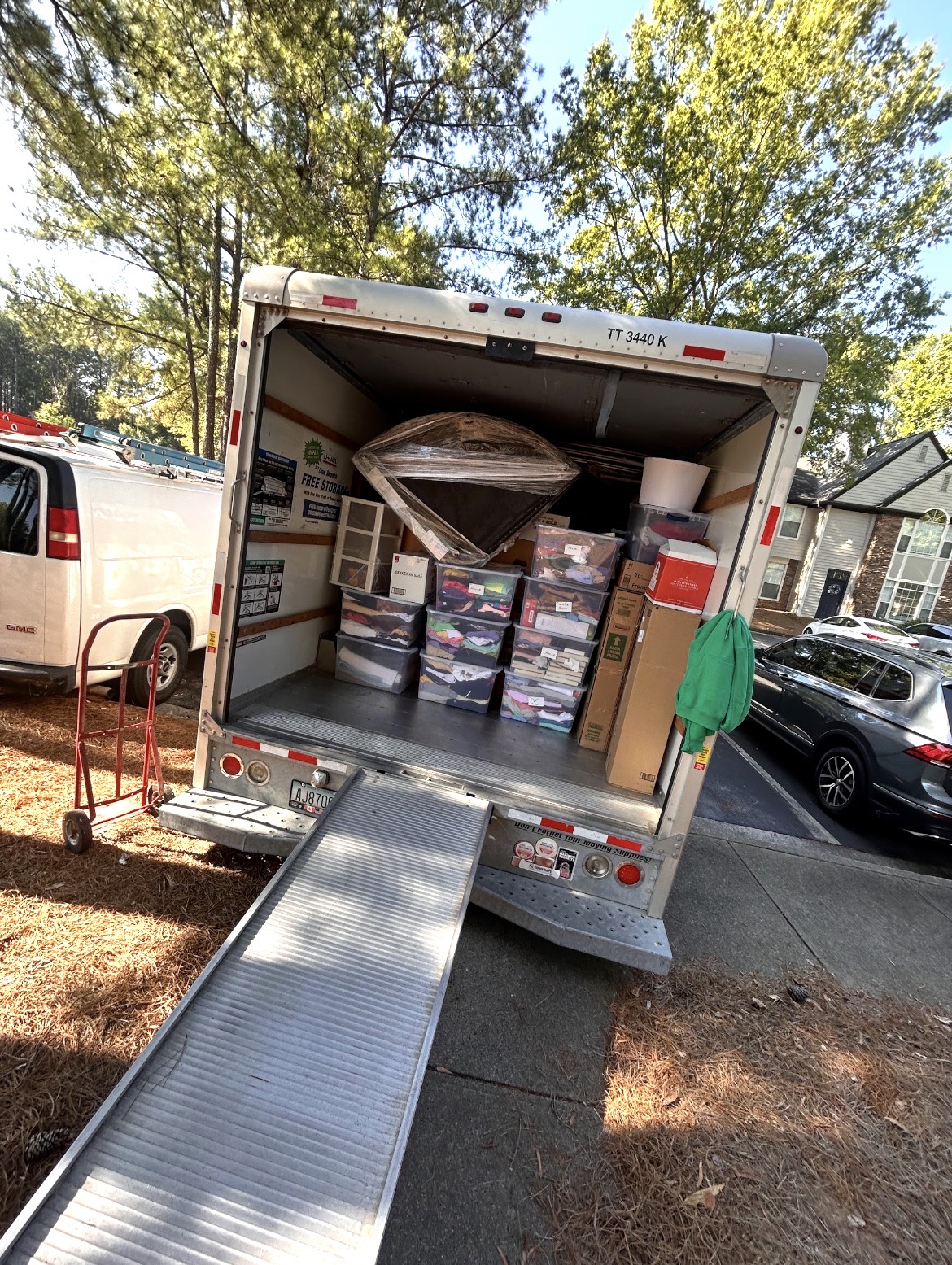 Open moving truck with boxes, storage bins, wrapped furniture, and an extended loading ramp