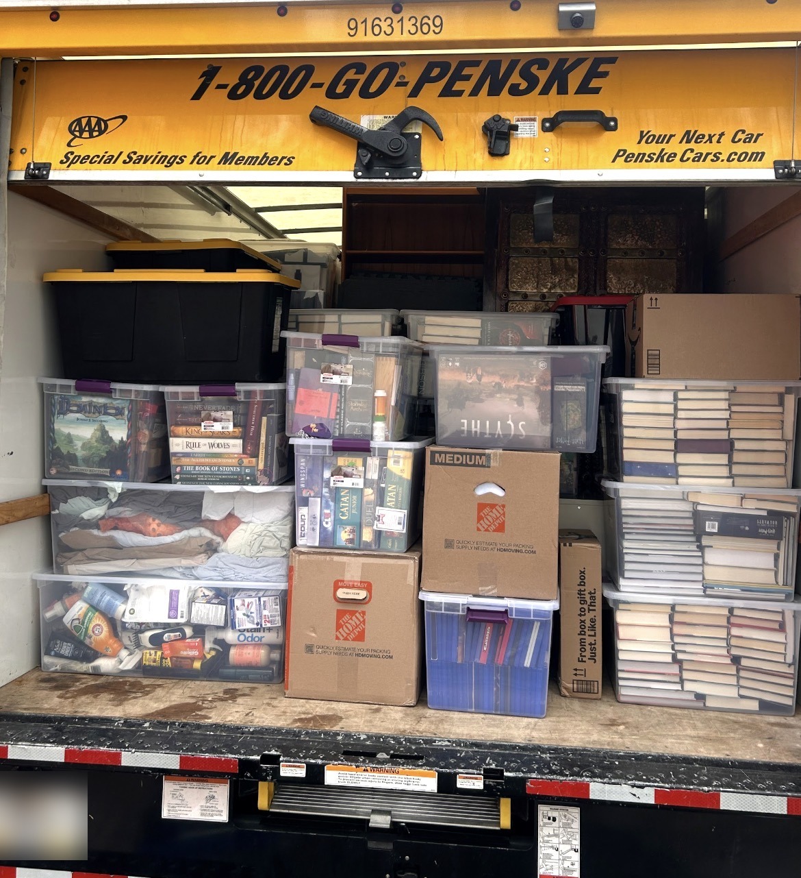 Open moving truck packed floor to ceiling with boxes, storage bins, and boxed books