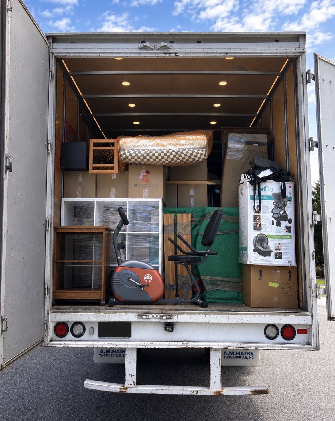 Open truck loaded with wrapped furniture, boxes, and an exercise bike